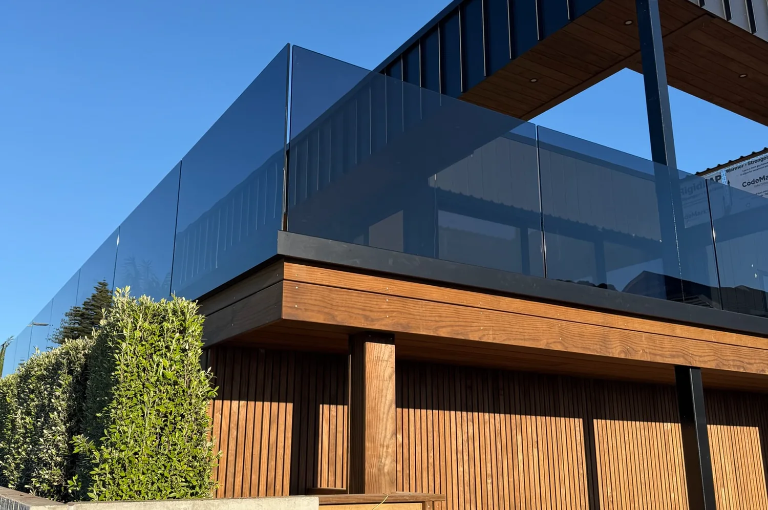 Frameless glass balustrade on the upper deck of a timber-clad home