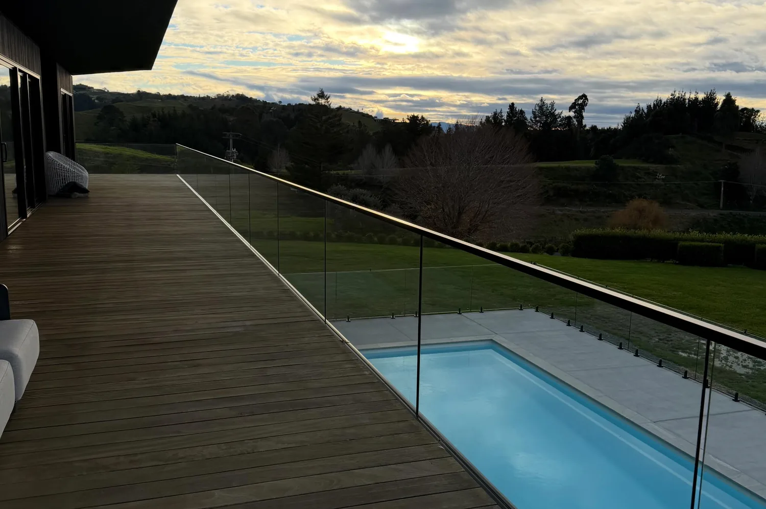 Frameless glass balustrade along a deck above a swimming pool at dusk