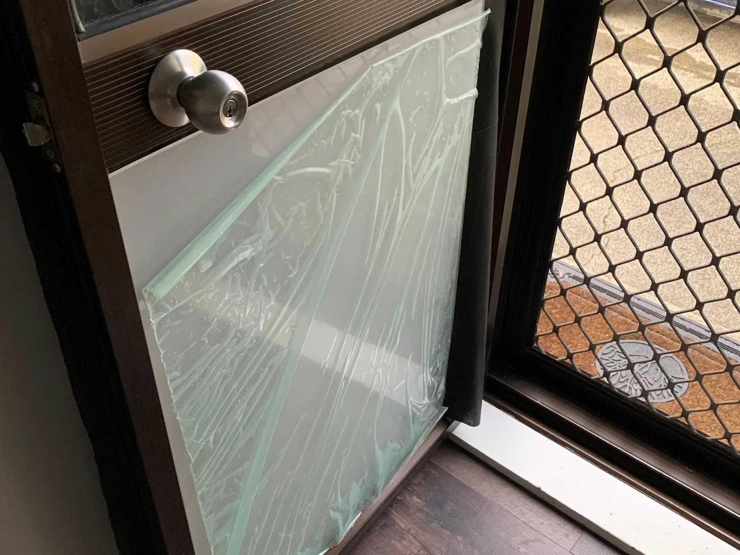 A shattered glass pane lifted out of a window frame, security mesh screen behind