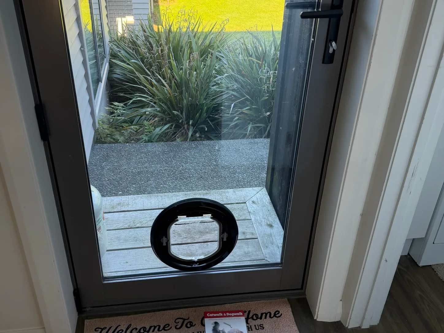 A round pet door fitted into a glass door beside the entry mat